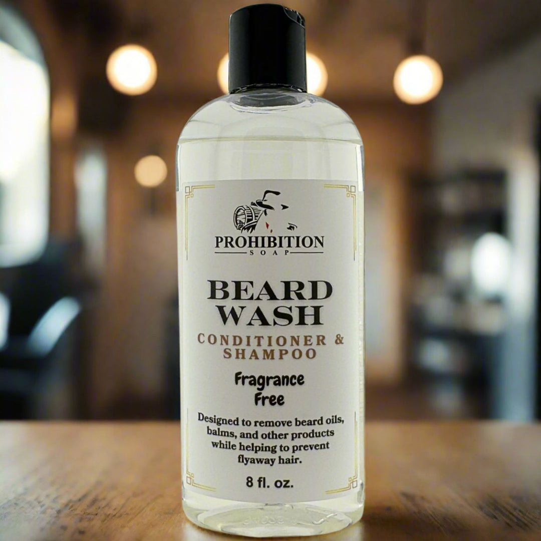 Prohibition Soap Fragrance Free Beard Wash conditioner and shampoo in clear 8 fl oz bottle with clear liquid on wooden surface in barbershop setting with warm lighting and blurred background, designed to remove beard oils and balms while preventing flyaway hair