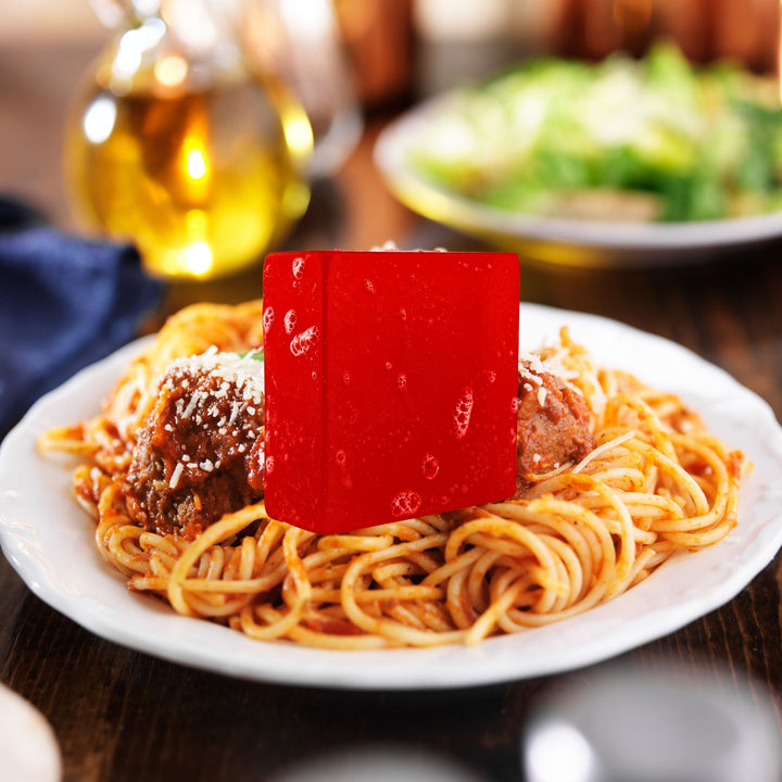 Plate of spaghetti with meatballs and a red bar of soap on a wooden table.