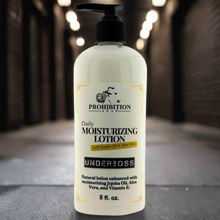 Prohibition Soap Daily Moisturizing Lotion in Underboss scent with 8 fl oz pump bottle on concrete surface with dramatic warm bokeh lighting in background, showing sophisticated cedarwood, tobacco and bourbon fragrance with jojoba oil, aloe vera and vitamin E
