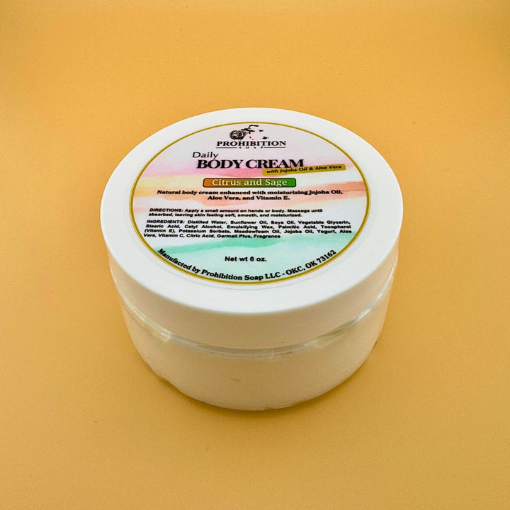 Prohibition Soap Daily Body Cream in white jar with Citrus and Sage scent label, showing natural yogurt base formula with jojoba oil and aloe vera, photographed on golden yellow background