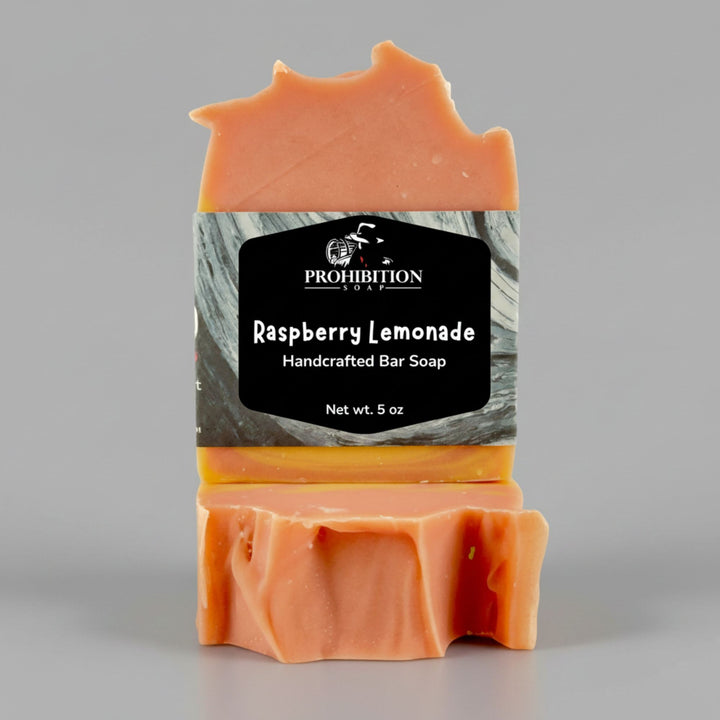 A handcrafted bar of soap with a rustic, jagged top, colored in shades of orange and yellow. It features a black and gray label with the brand name &