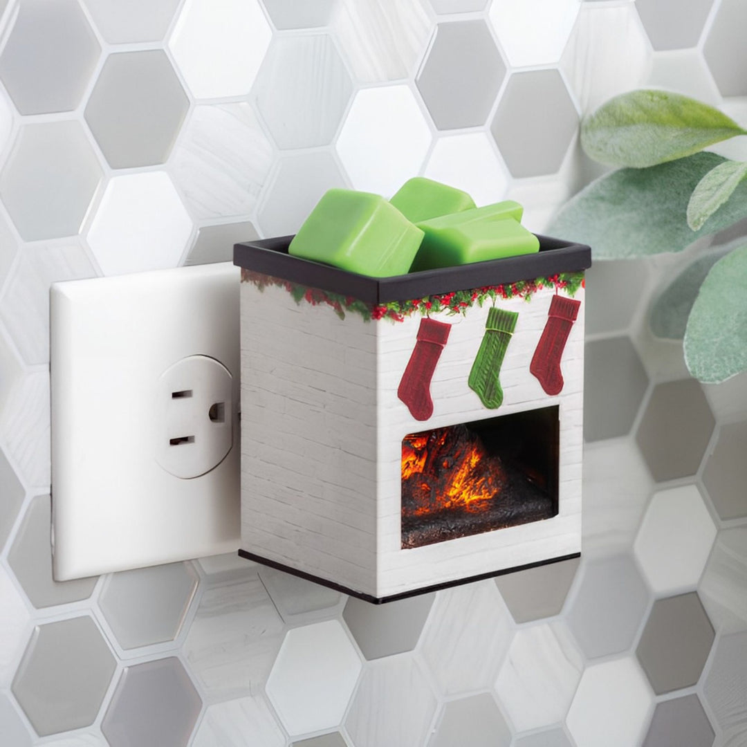 Decorative electric fireplace fragrance warmer with stockings and green wax melts next to a wall outlet on a hexagonal tile background.