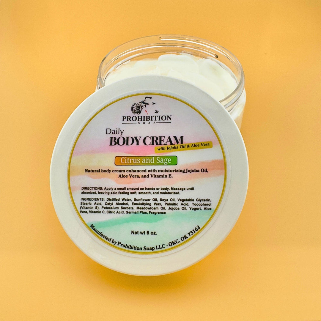 Prohibition Soap Daily Body Cream jar opened to show thick white cream texture with full product label visible, featuring Citrus and Sage scent with jojoba oil and aloe vera on golden yellow background