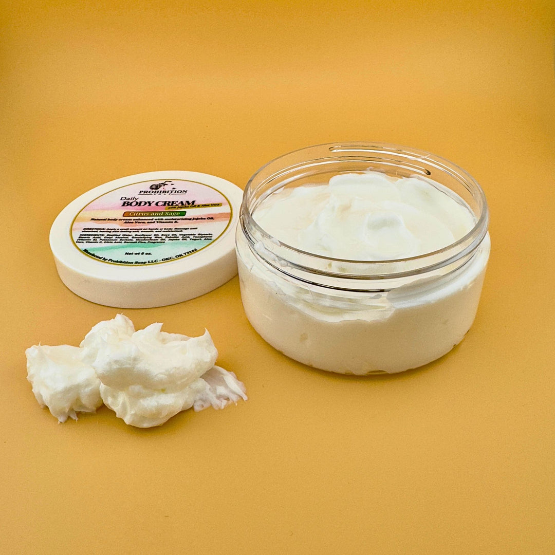 Prohibition Soap Daily Body Cream open jar showing thick white cream texture with lid and scooped portion displayed, featuring Citrus and Sage scent with natural yogurt base formula on golden yellow background