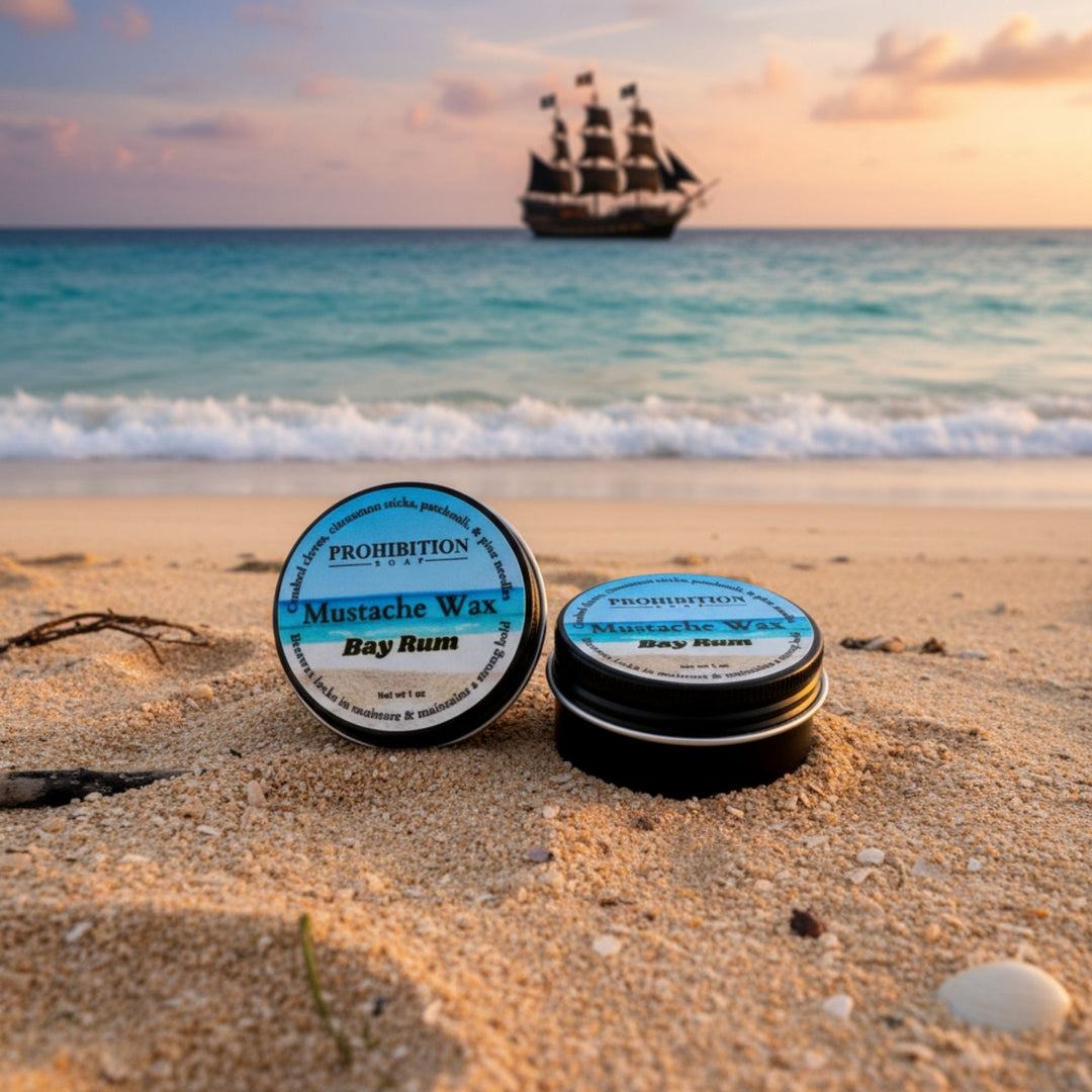 Two containers of Prohibition Mustache Wax on a beach with a pirate ship in the background.