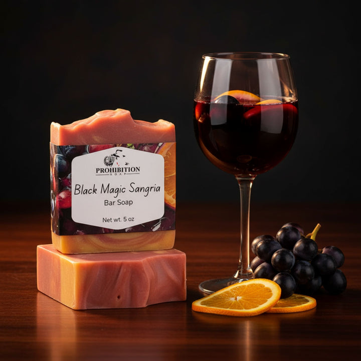 Bar soap labeled 'Black Magic Sangria' next to a glass of red wine and grapes on a dark background