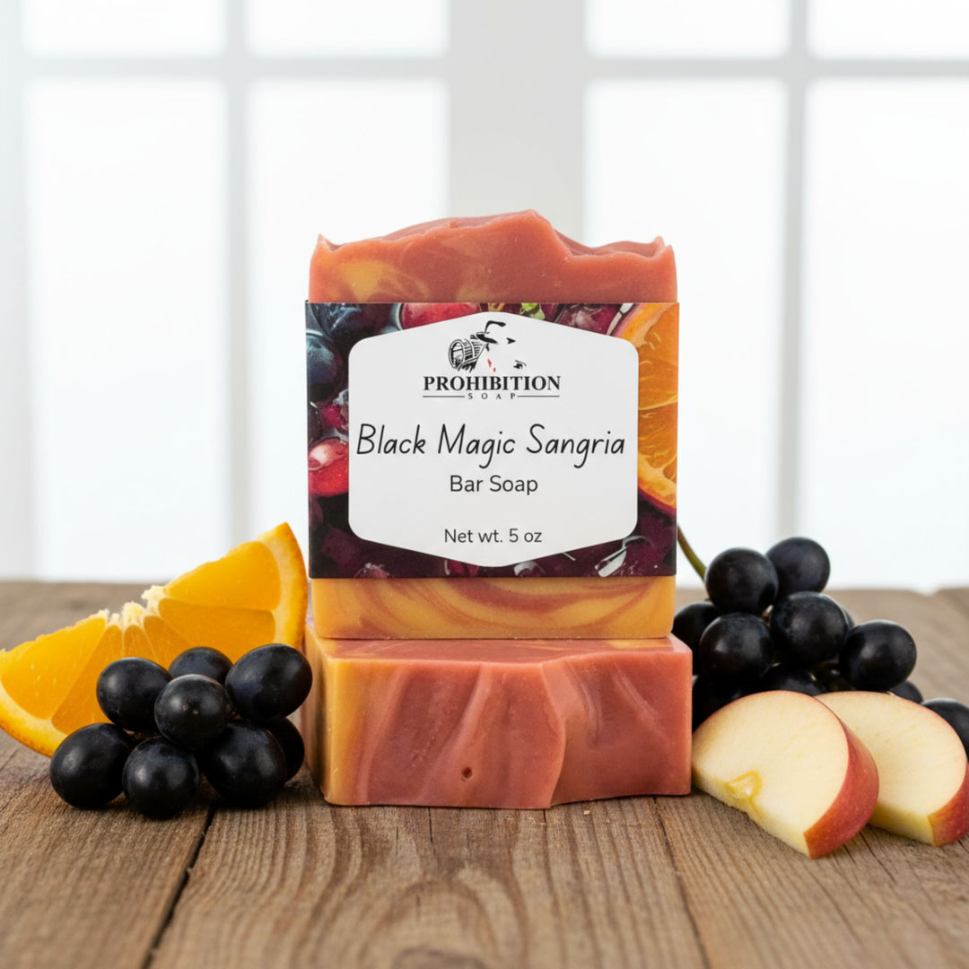 Bar of soap with 'Black Magic Sangria' label surrounded by fruits on a wooden surface
