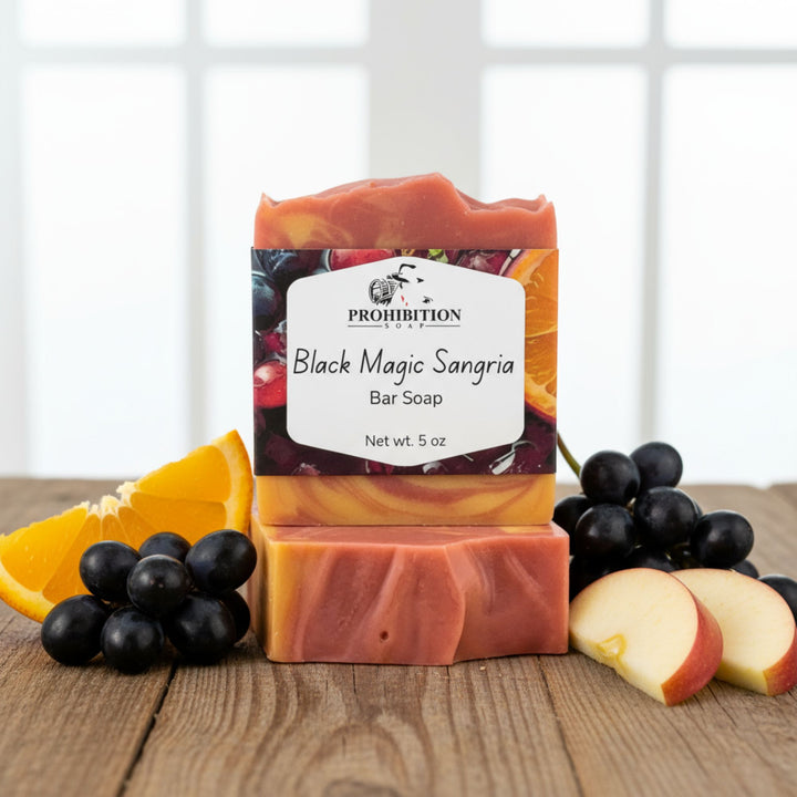 Bar of soap with 'Black Magic Sangria' label surrounded by fruits on a wooden surface