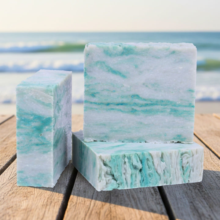Marble-patterned soap bars on a wooden surface with a blurred beach background