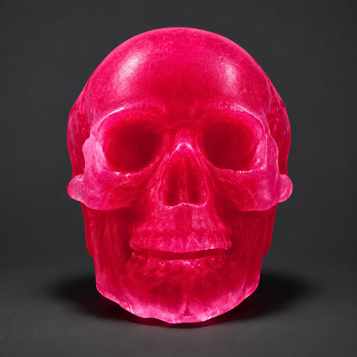 A translucent hot pink skull soap, centered against a dark gray studio background.