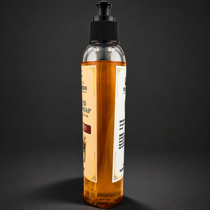 A clear plastic pump bottle filled with amber-colored soap, standing upright against a dark gray background. The bottle has a black ribbed pump cap and a cream-colored label with black text.