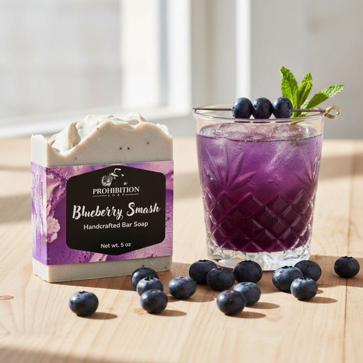 Prohibition Blueberry Smash soap bar with a purple cocktail and blueberries on a wooden surface