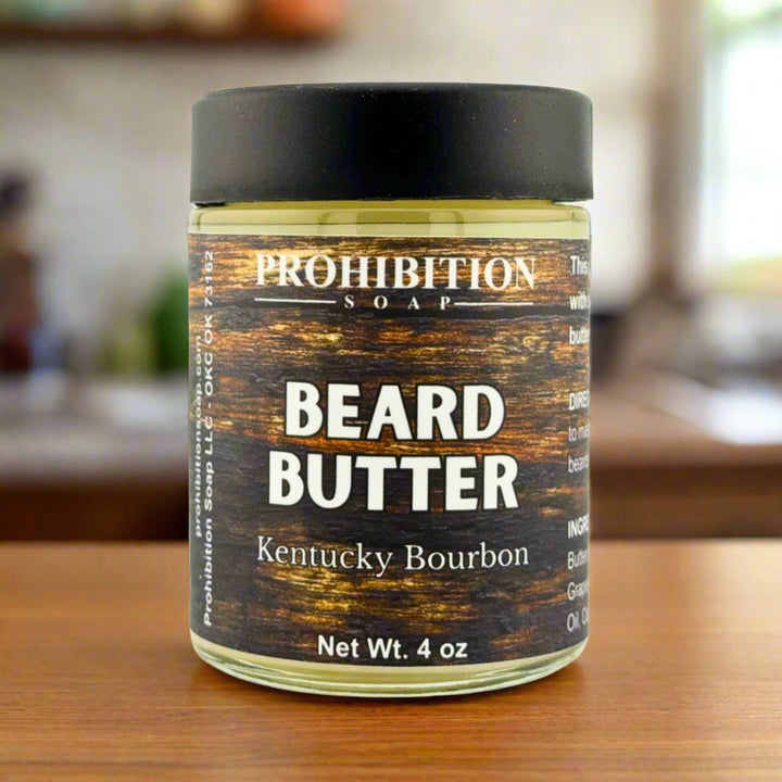 Prohibition Soap Beard Butter in Kentucky Bourbon scent - 4 oz glass jar on wooden surface with warm home interior background, showing rich wood grain textured label design with bourbon barrel aesthetic