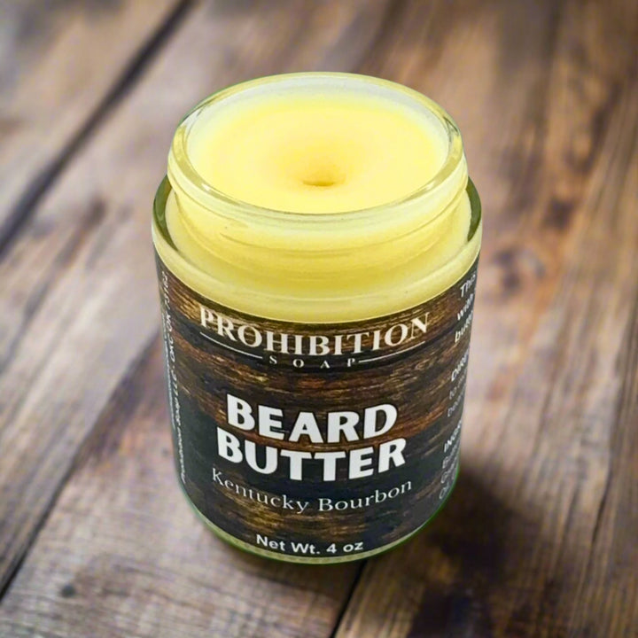 Prohibition Soap Beard Butter in Kentucky Bourbon scent - open 4 oz glass jar showing rich golden butter texture and consistency with wood grain textured label on rustic wooden surface