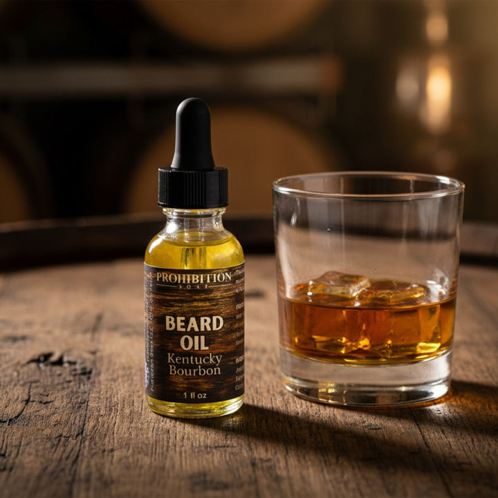 Dropper bottle of Prohibition Beard Oil Kentucky Bourbon next to a glass of whiskey on a wooden surface.