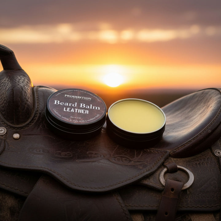 Two containers of 'Prohibition' beard balm on a leather saddle with a sunset background.