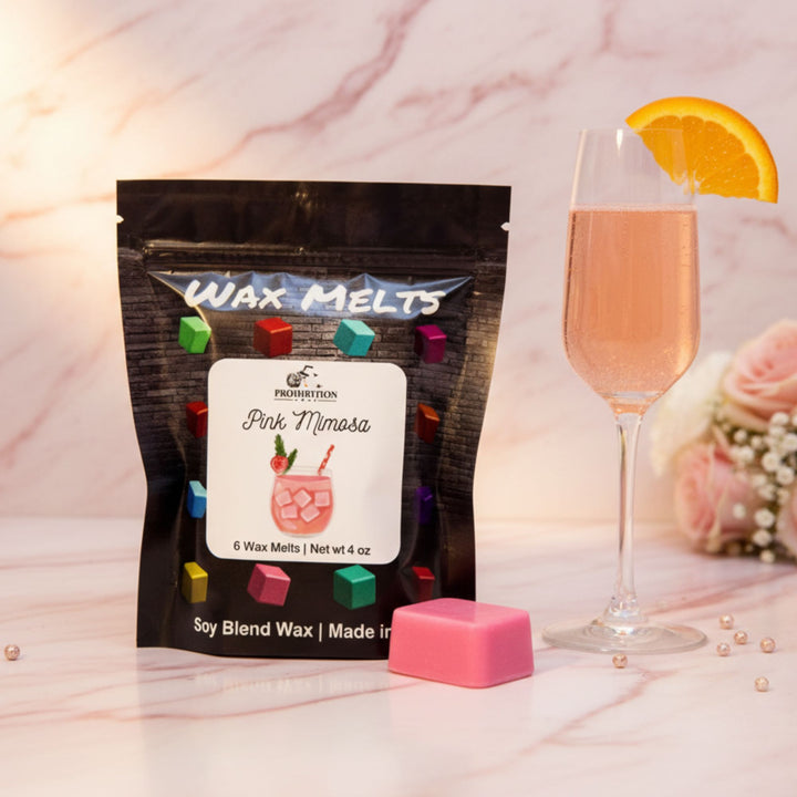 Packaging of Pink Mimosa wax melts with a glass of pink drink and orange slice on a marble surface.