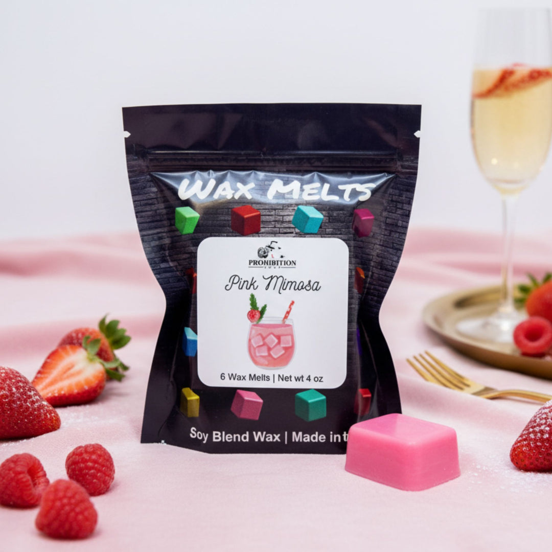 Packaged wax melts with a pink mimosa design on a pink surface with strawberries and a glass of champagne.