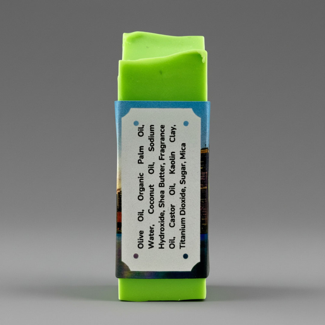 A rectangular handmade soap bar wrapped in a blue paper band with a white ingredient label, photographed against a neutral gray background.