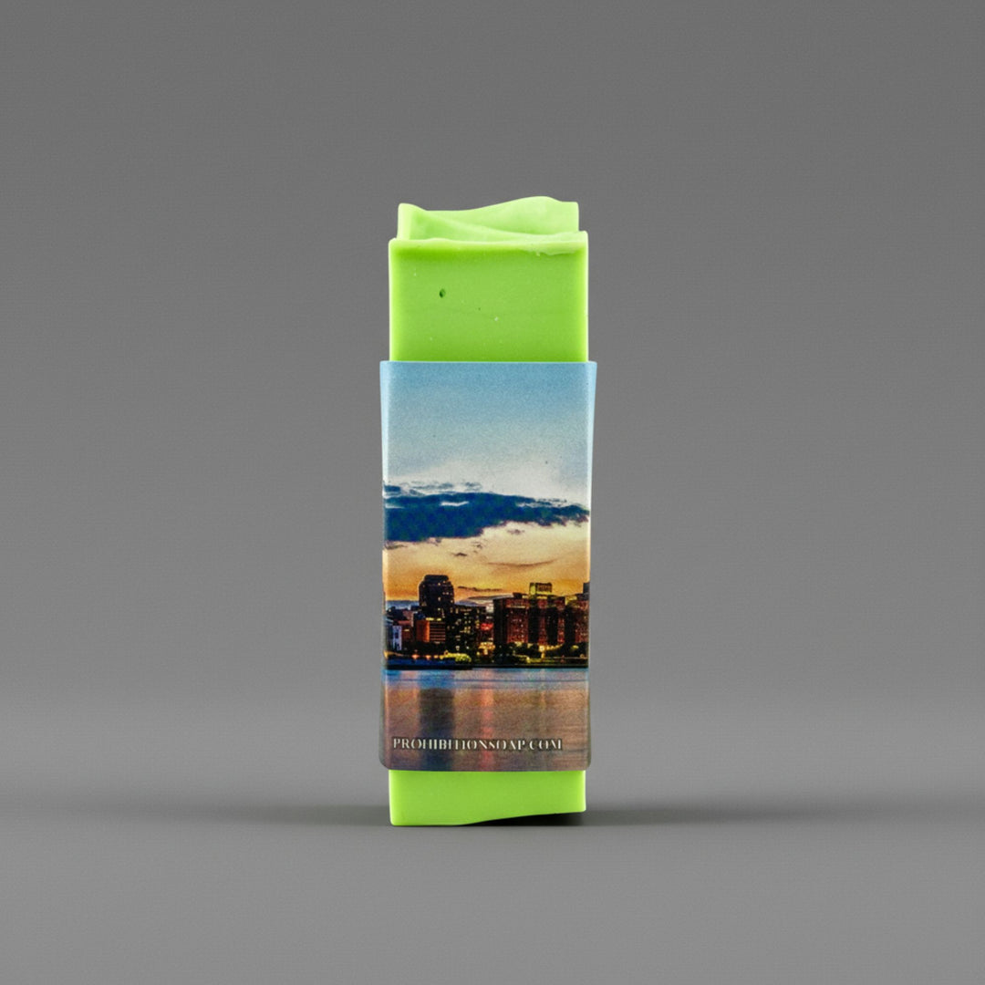 A bright lime green rectangular bar wrapped in a printed paper sleeve showing a city skyline at sunset, centered on a smooth gray background.