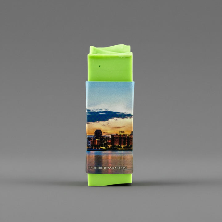 A bright lime green rectangular bar wrapped in a printed paper sleeve showing a city skyline at sunset, centered on a smooth gray background.
