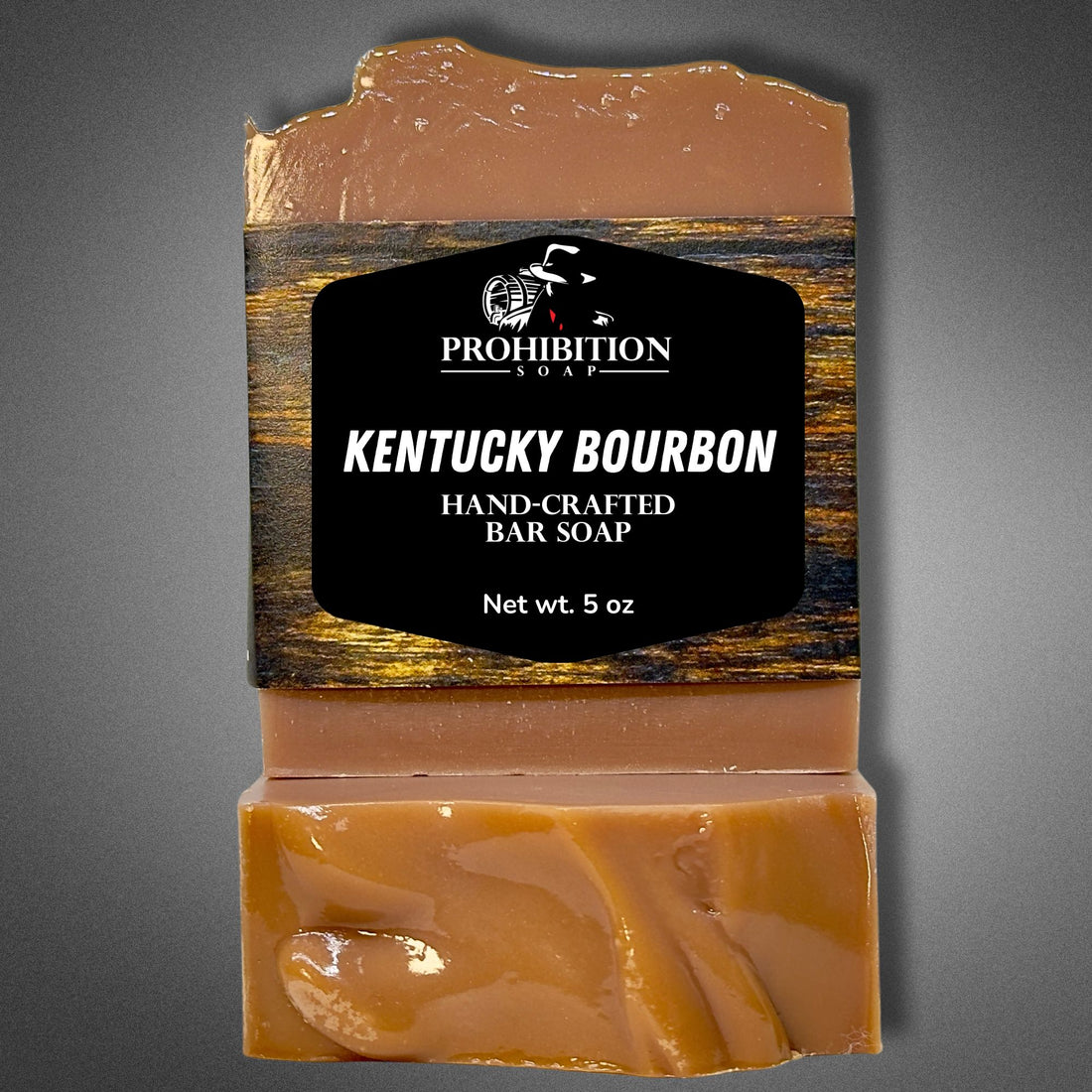 Kentucky Bourbon bar soap with Prohibition Soap label standing beside two unwrapped bars stacked to show the swirled amber interior, on a gray background