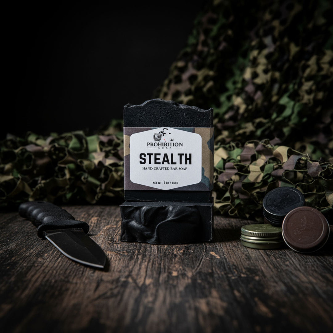 Bar of soap labeled 'Stealth' with a knife and cammie paint on a wooden surface with camouflage fabric in the background.