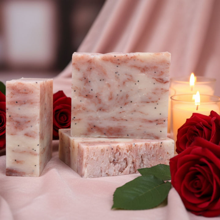 Three bars of soap with red roses and a lit candle on a soft pink background