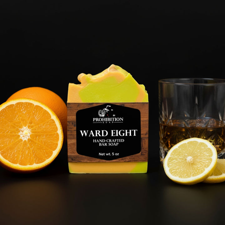 Hand-crafted bar soap with label, half an orange and lemon, and a glass of whiskey on a dark background.